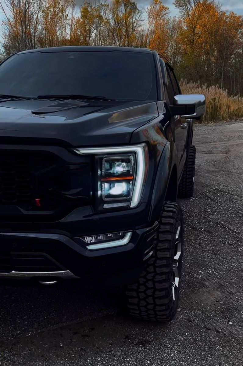 Front of Nick's black Ford F150 with autumn trees behind it