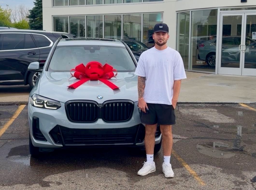 Nick next to the new BMW with a red bow at the dealership